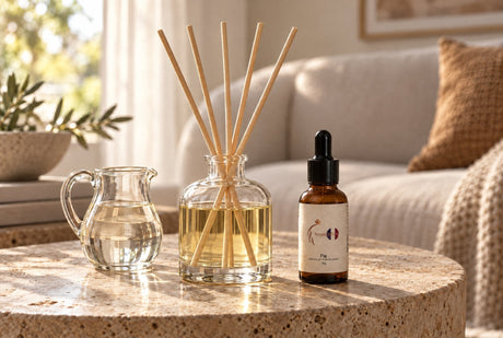 Glass reed diffuser with five rattan reeds beside a jug of diffuser base and a Scent DNA Fig perfume oil bottle on a stone side table