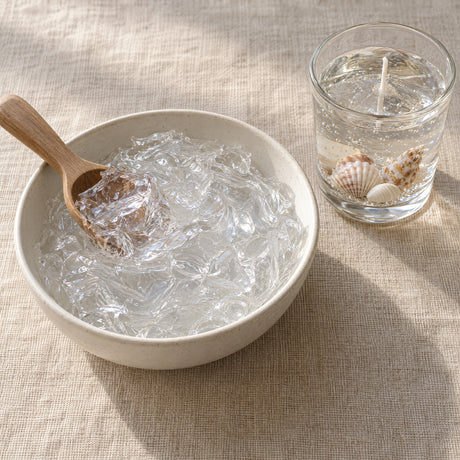 Clear gel wax in a shallow bowl with a wooden scoop, seen from above on a linen surface