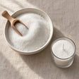 Sand wax granules in a shallow bowl with a wooden scoop, seen from above on a linen surface