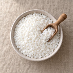 Soy pillar wax beads in a shallow bowl with a wooden scoop, seen from above on a linen surface