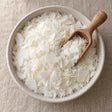 Soy wax flakes in a shallow bowl with a wooden scoop, seen from above on a linen surface
